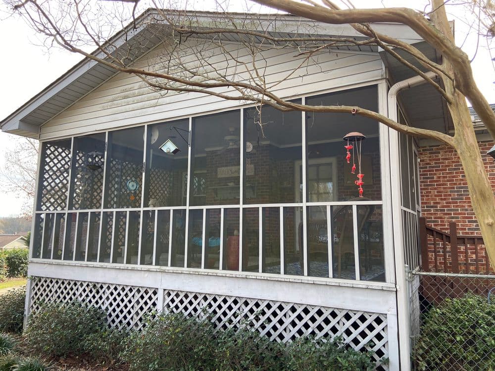 Screened porch with brick exterior, decorative hanging items, and surrounding greenery.