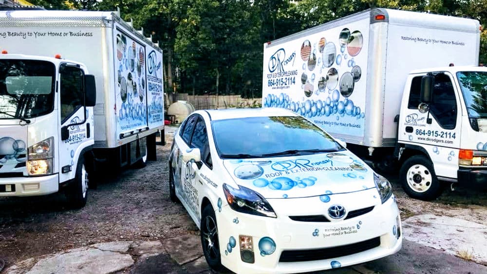 Branded vehicles for roof maintenance services parked at a business location.