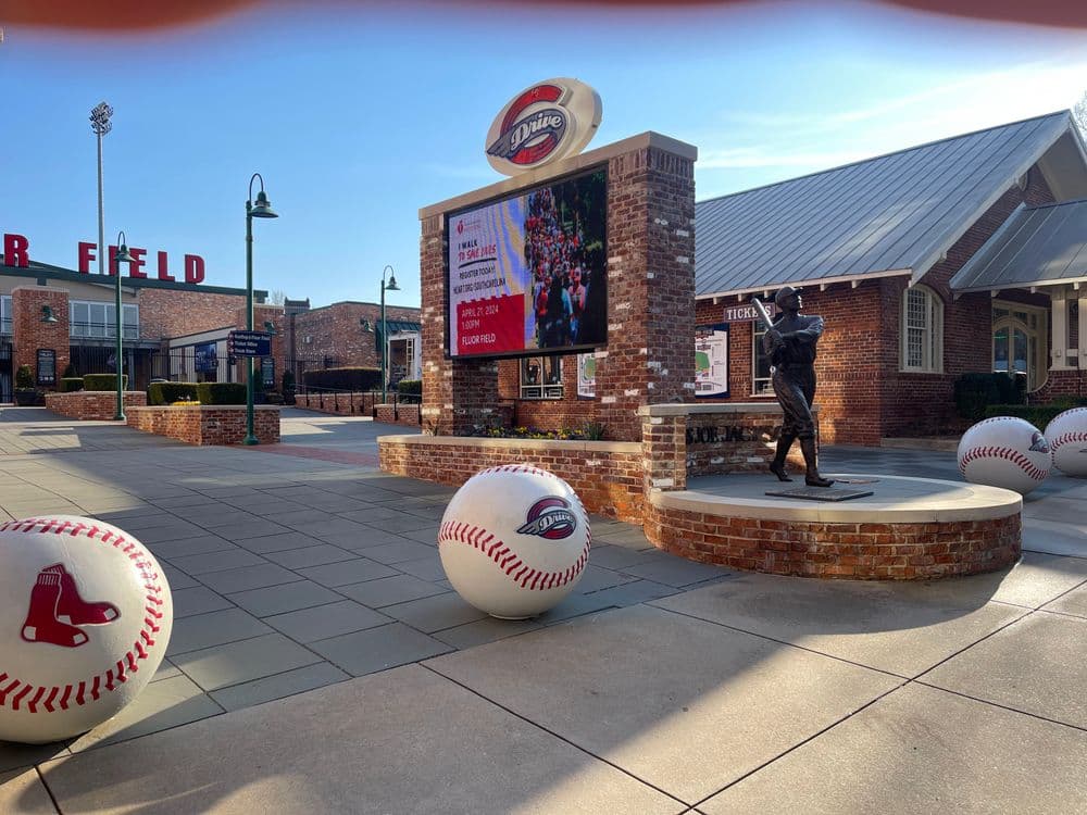 Baseball park entrance with large balls and a statue, featuring a digital display.