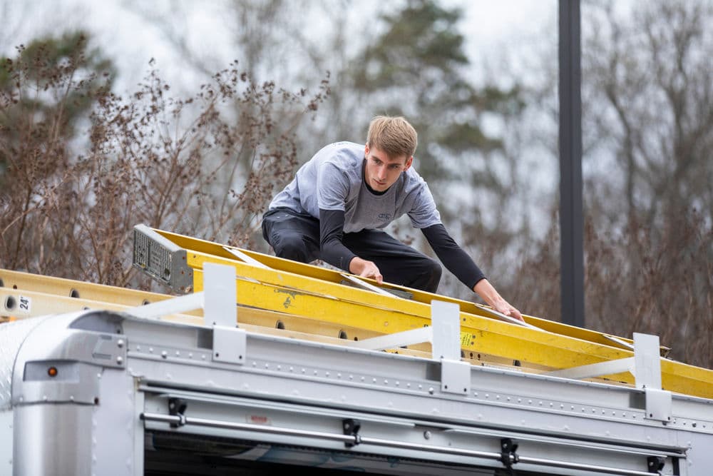 Worker maneuvering on a yellow ladder atop a moving truck during a relocation service.