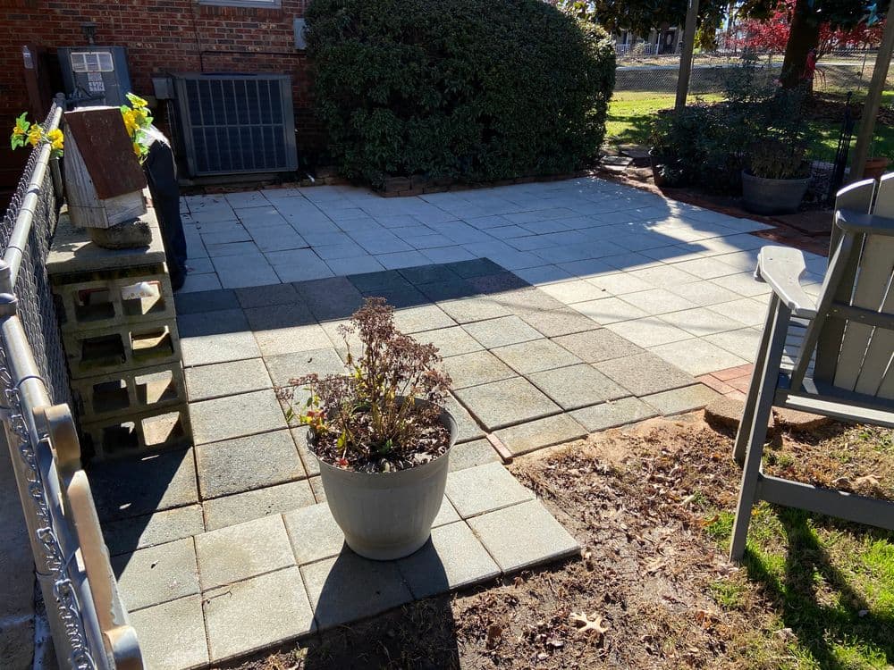 Paved outdoor patio area with a potted plant and landscaping features, under clear skies.
