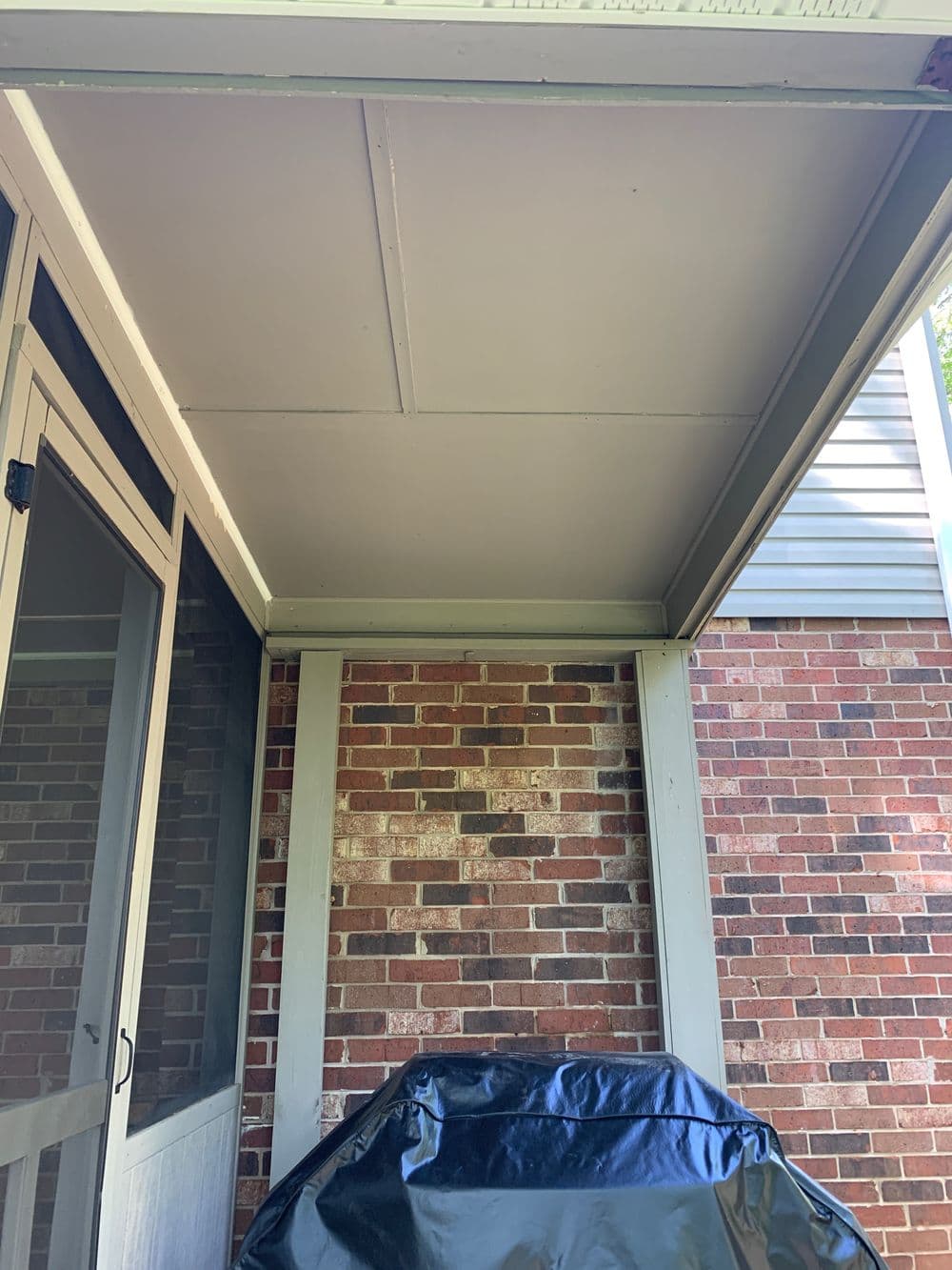 Covered patio with a grill, featuring brick walls and a screened-in area.