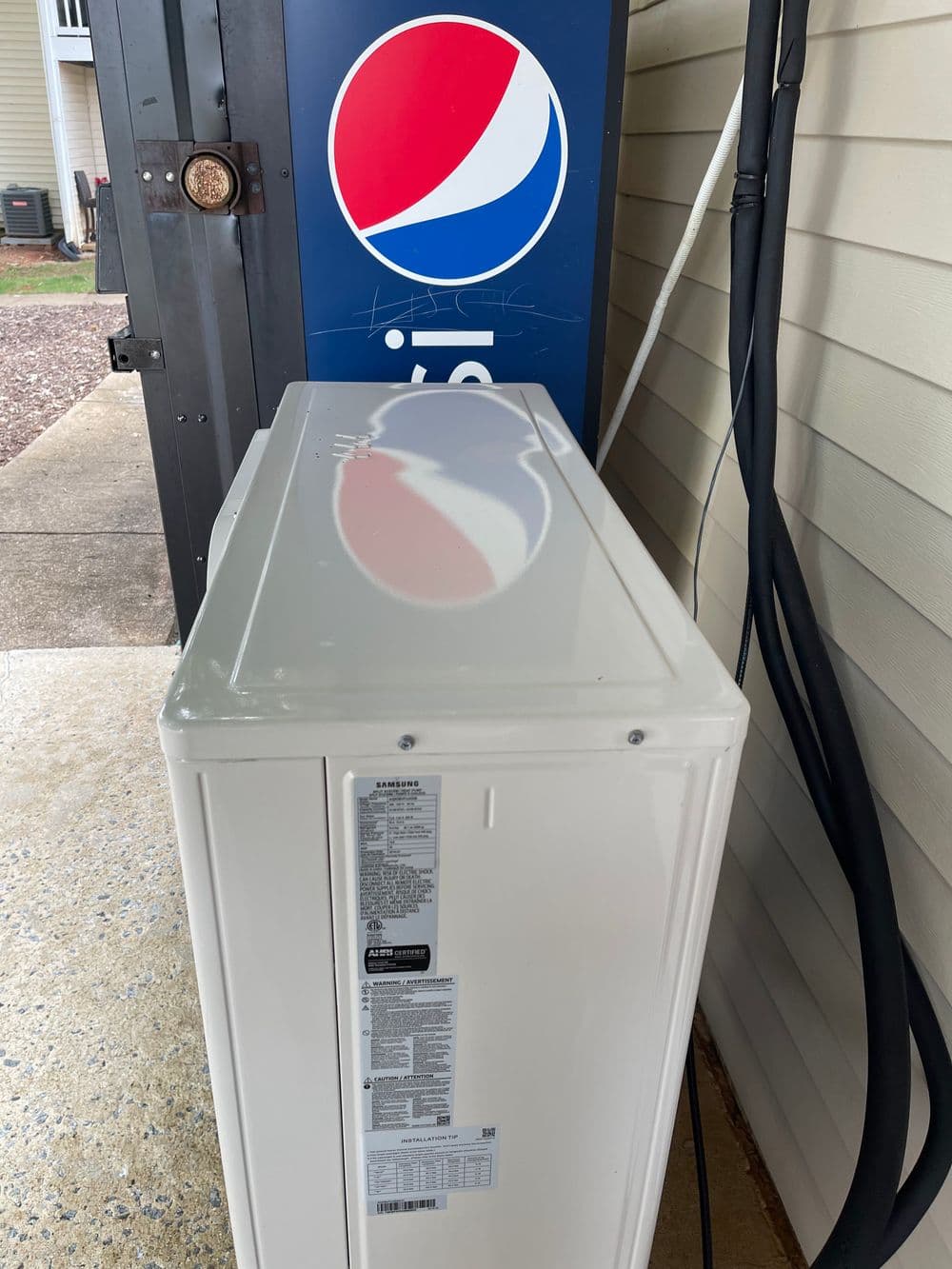 White refrigerator next to a Pepsi vending machine outside a building.
