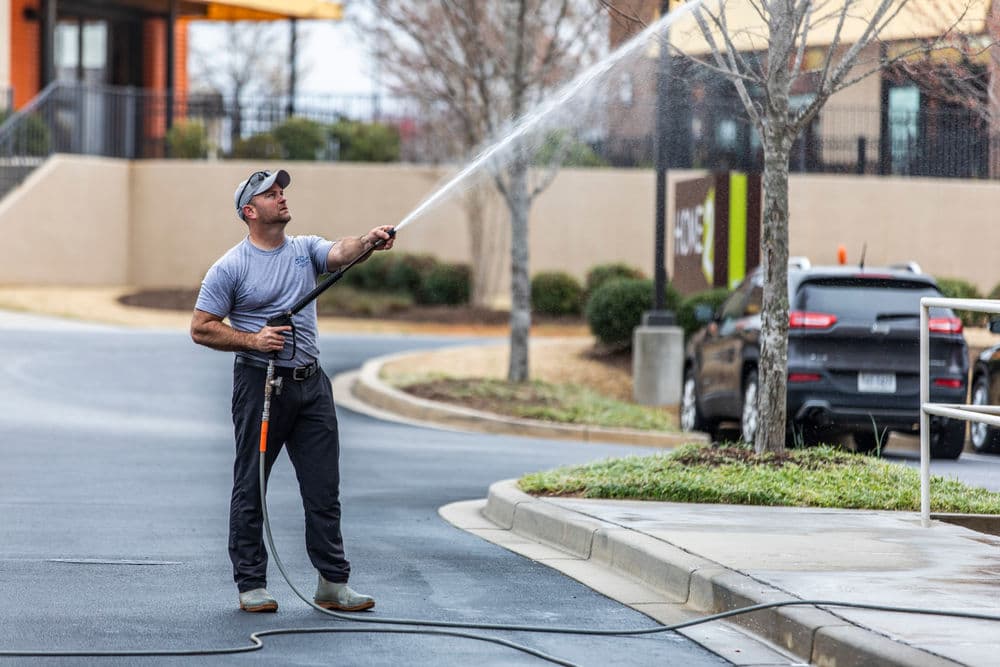 Man using a pressure washer on a sidewalk, maintaining cleanliness in an outdoor setting.