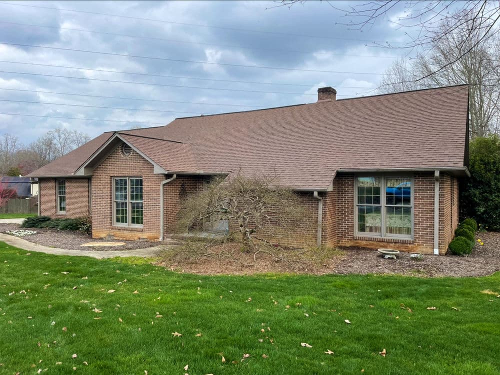 Single-story brick house with a manicured lawn and large windows under cloudy skies.