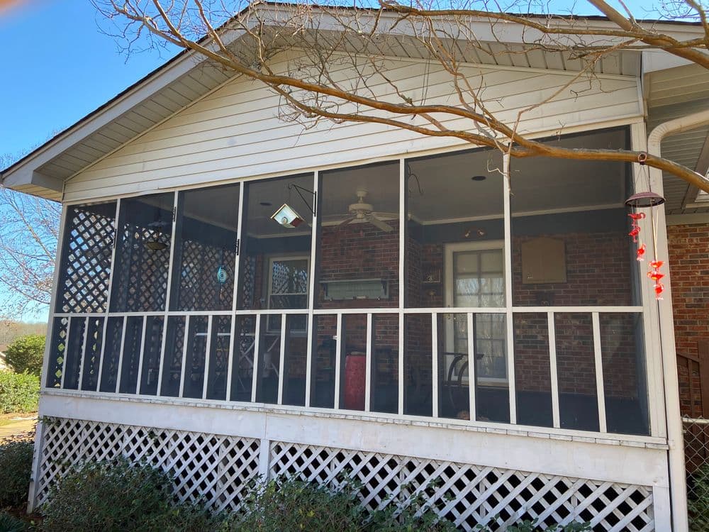 Screened porch with latticework, brick interior, and ceiling fan, surrounded by greenery.