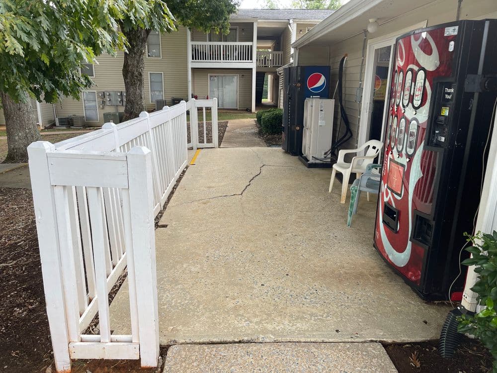 Vending machines near apartment complex with white fence and seating area.