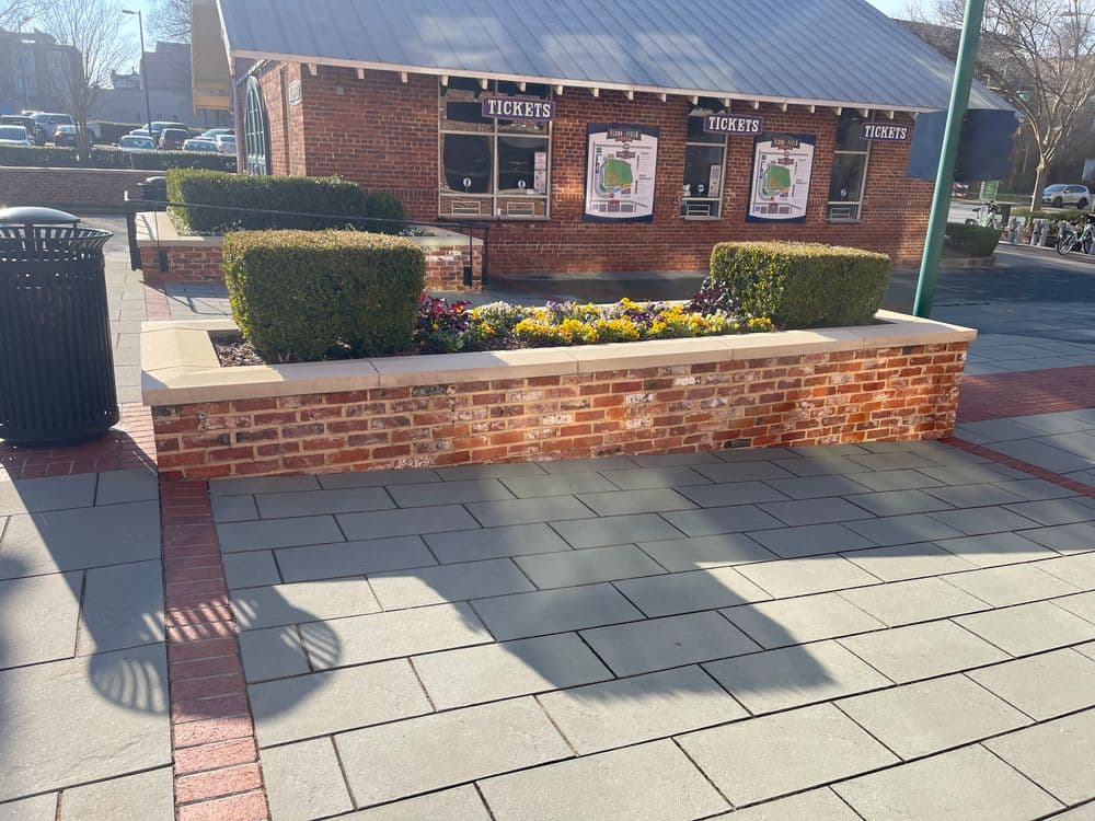 Ticket booth surrounded by flower beds in a brick plaza on a sunny day.