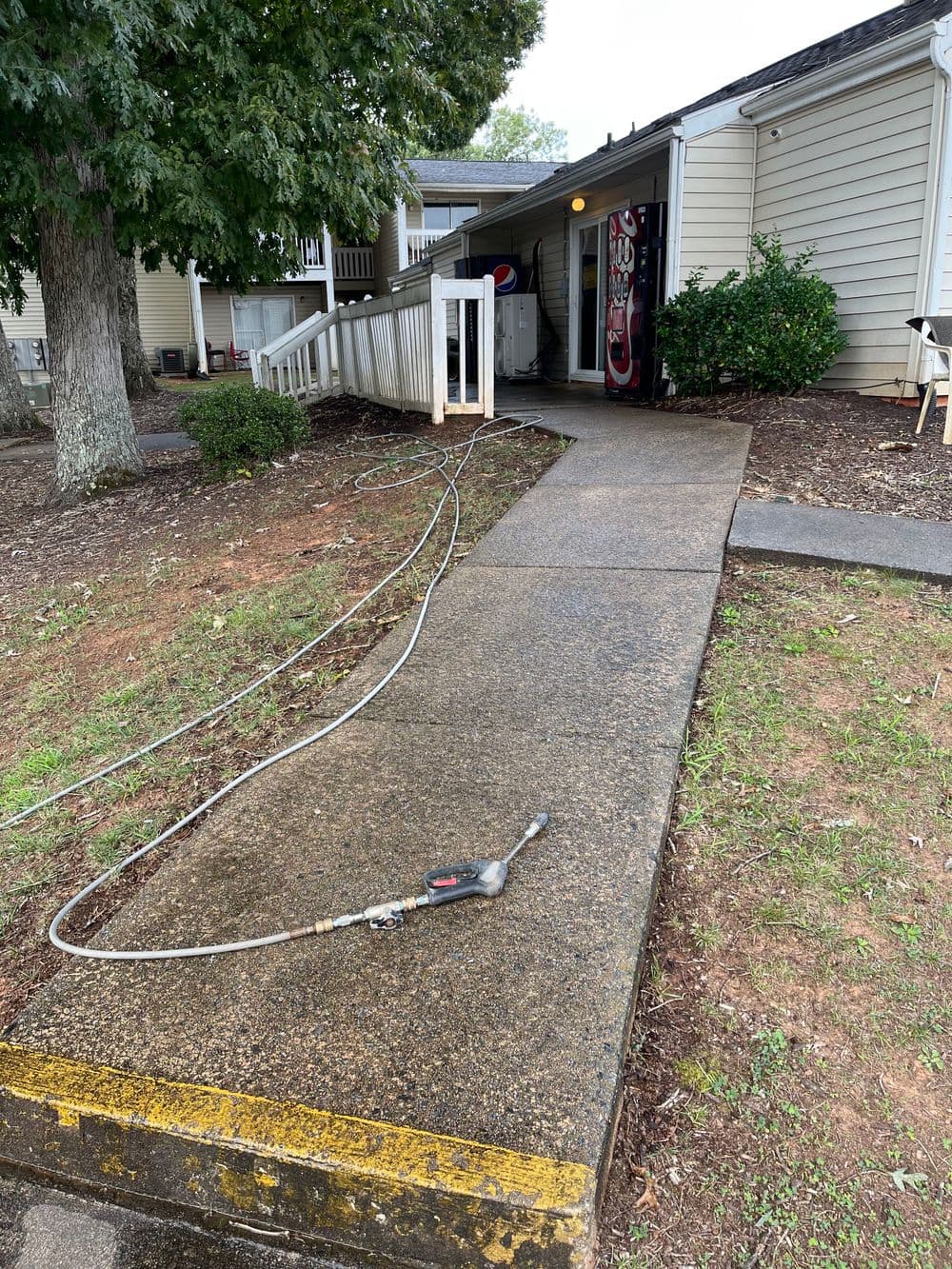 Concrete walkway leading to a building entrance, with a pressure washer hose and vending machine nearby.