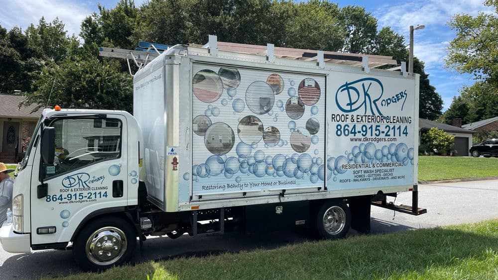 Truck for DK Roof & Exterior Cleaning parked on residential street, featuring logo and contact info.