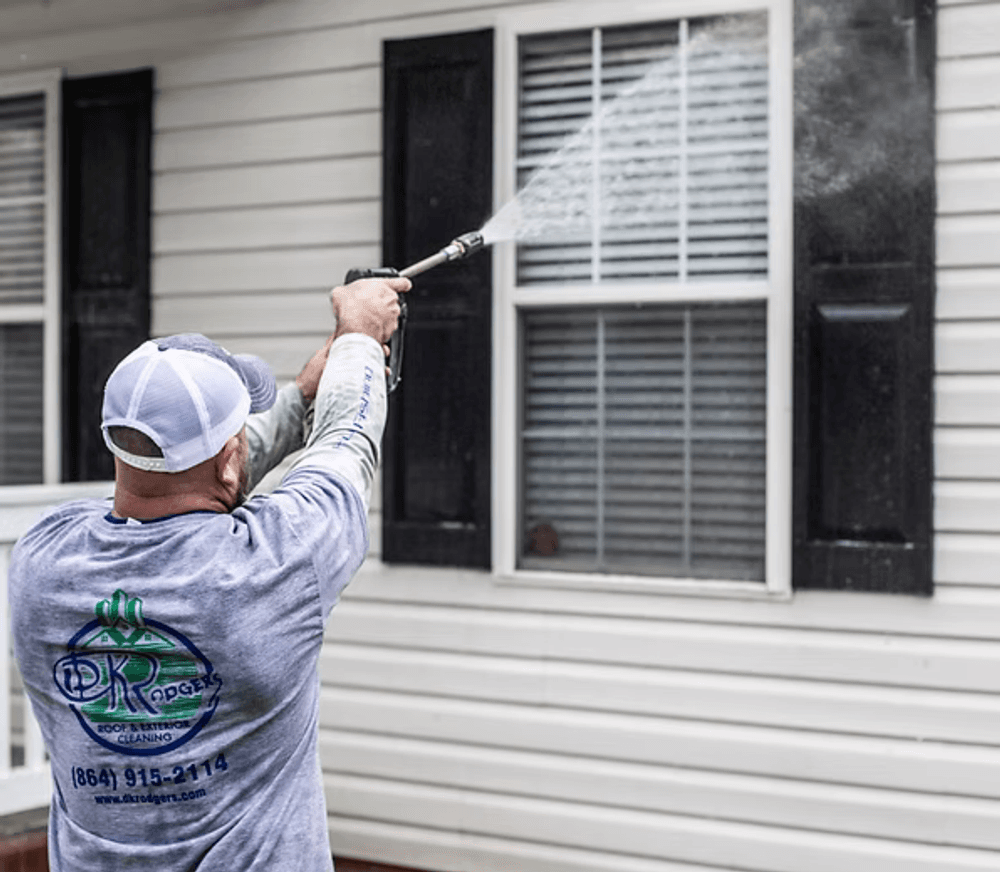 Professional pressure washing technician cleaning residential siding and window outdoors.
